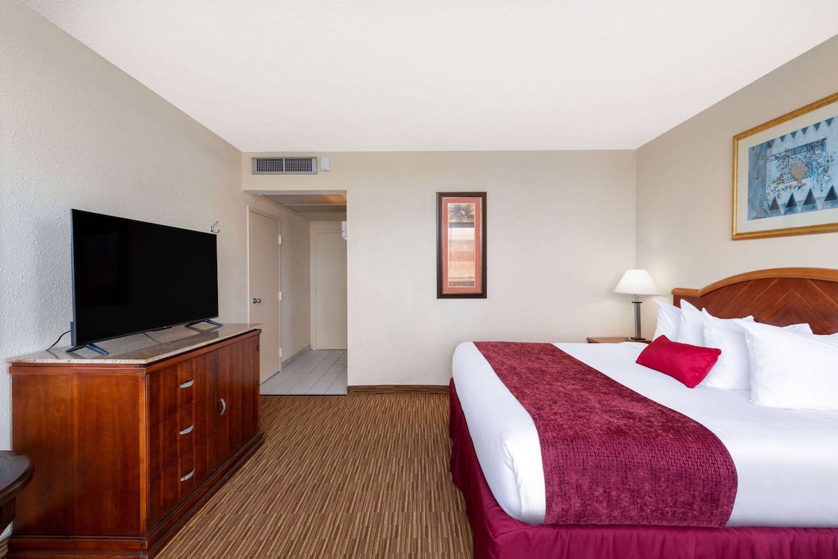 A hotel room with a bed, a TV on a wooden cabinet, a painting on the wall, and a door leading to another room.