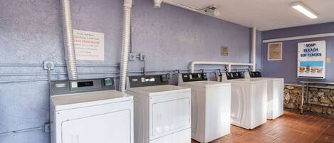 A laundry facility with multiple washing machines, a sign about soap and bleach softeners, and a stone wall.