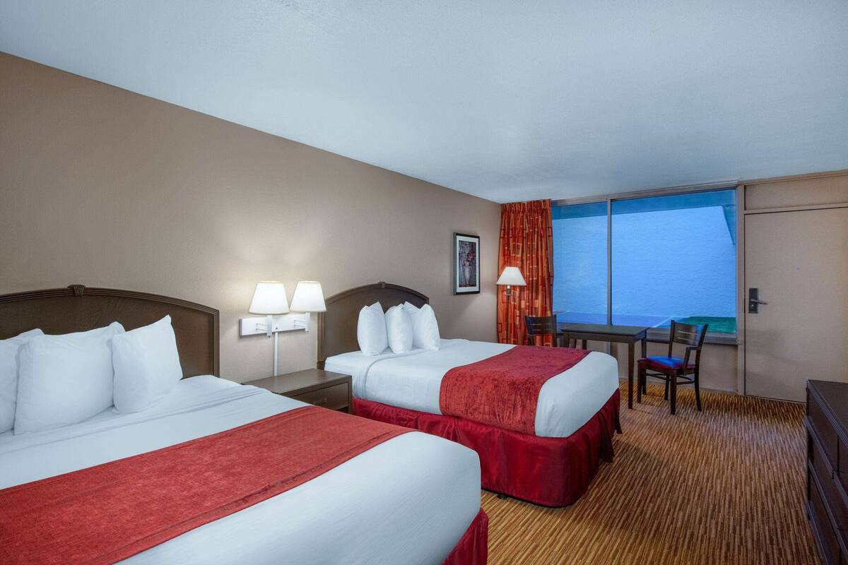 A hotel room with two beds, a desk, a chair, and a large window with curtains.