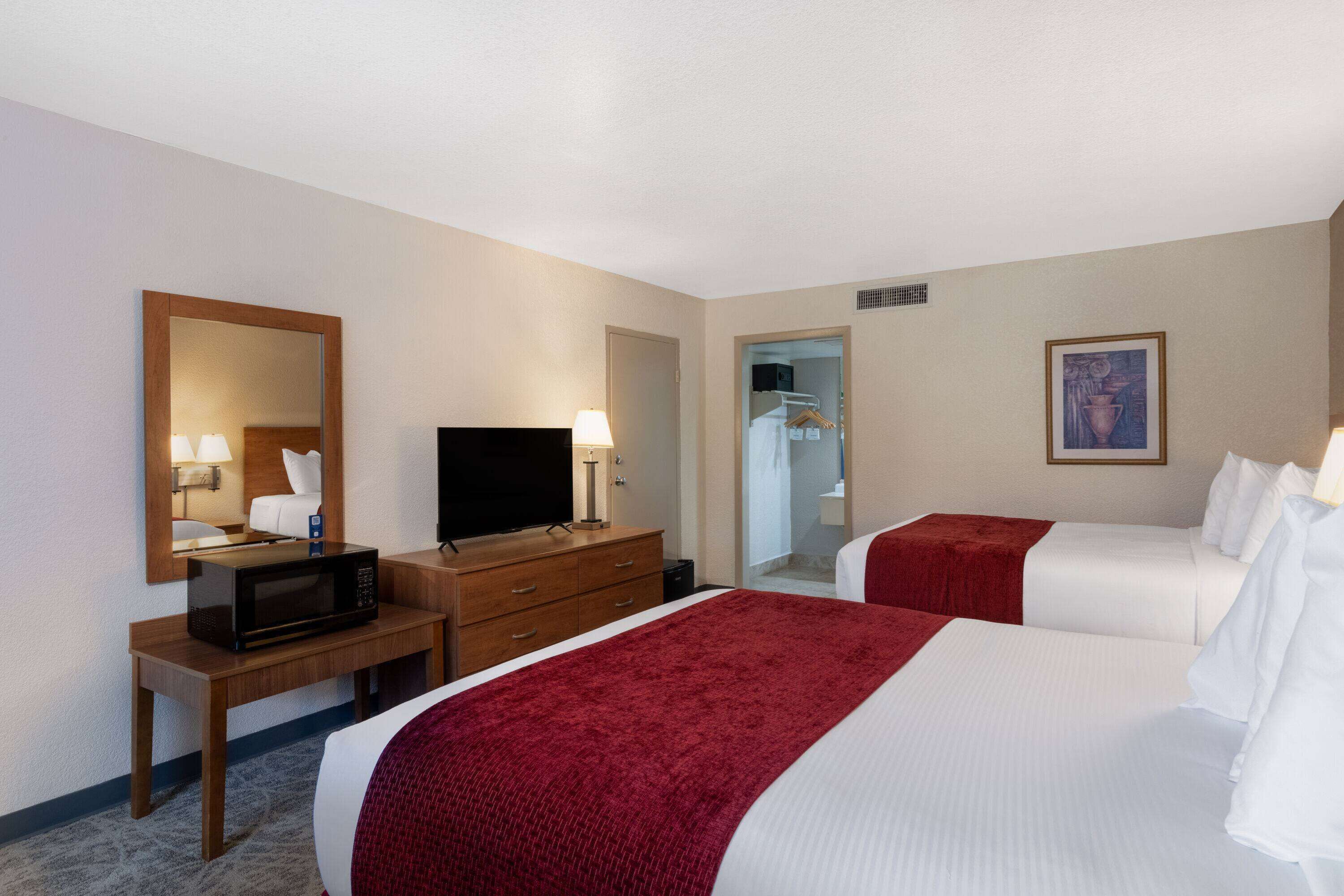 Una habitación de hotel con dos camas, un televisor, un escritorio con microondas y un espejo.