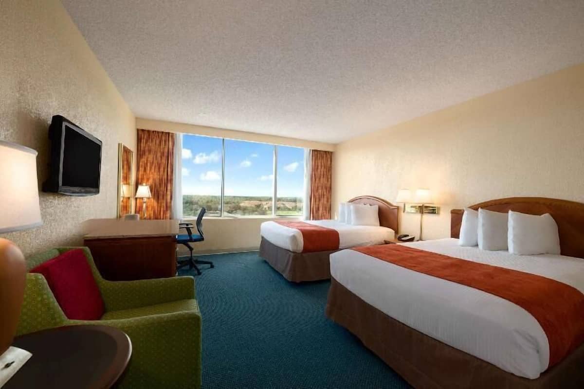 A hotel room with two beds, a desk, a chair, a TV, and a large window with a view.