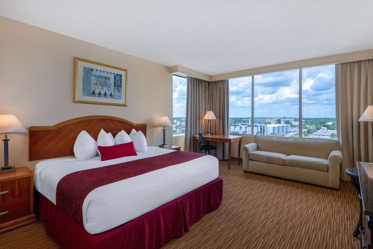A hotel room with a large bed, a desk, a sofa, and a view of the city.