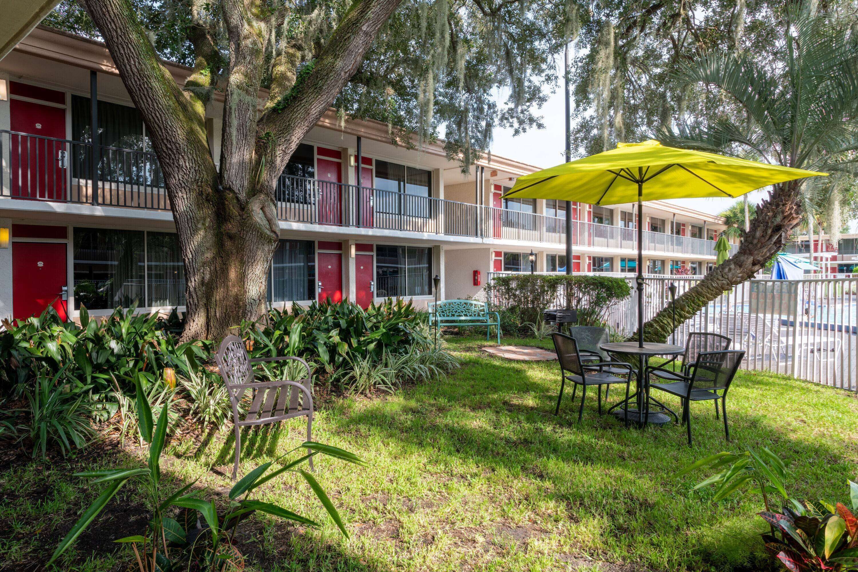 A hotel with a two-story structure, outdoor seating area with a yellow umbrella, and a well-maintained garden.