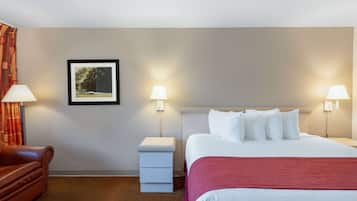 Une chambre d’hôtel avec un lit, deux lampes de chevet, une table de chevet, une chaise et un tableau encadré au mur.