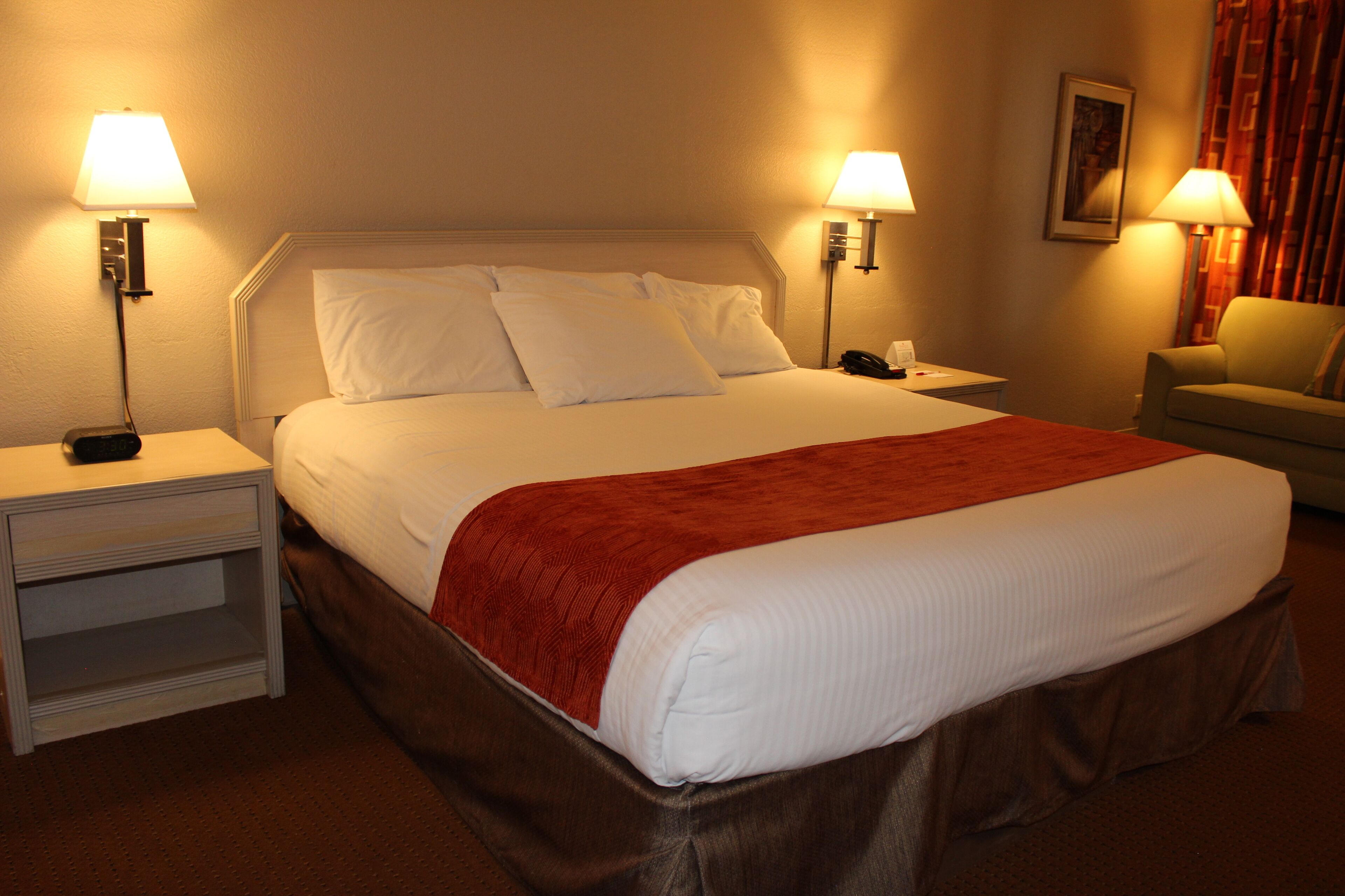 A hotel room with a large bed, two bedside tables, a chair, and two lamps.