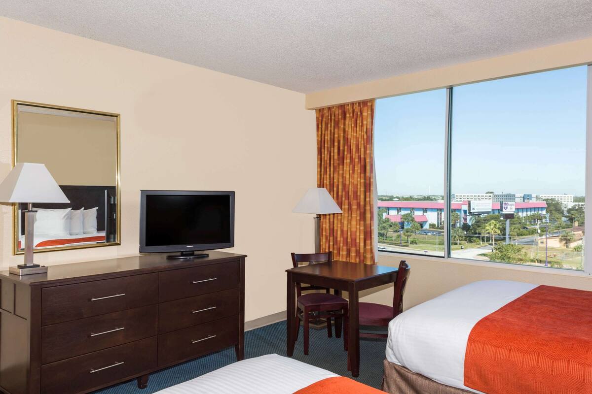 A hotel room with a bed, a desk, a television, and a window with a city view.