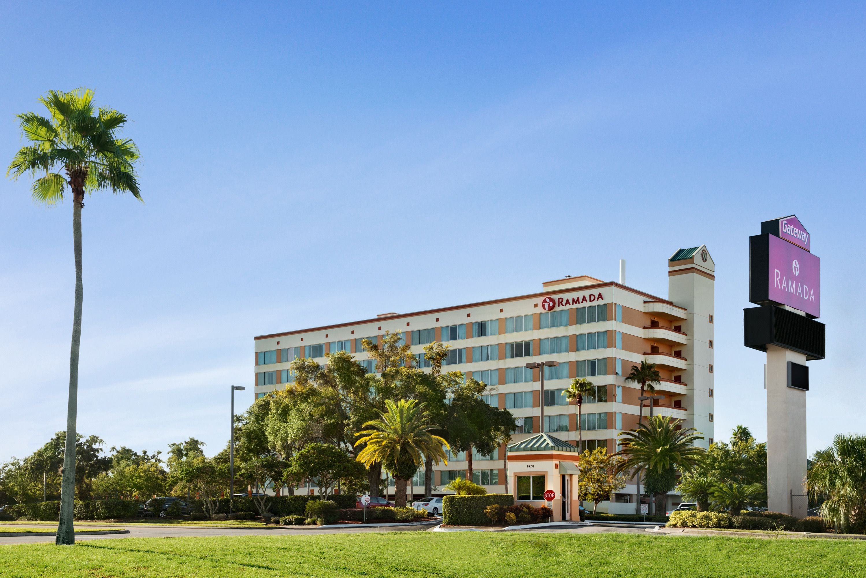 A multi-story hotel with a prominent "Ramada" sign, surrounded by palm trees and a clear sky.
