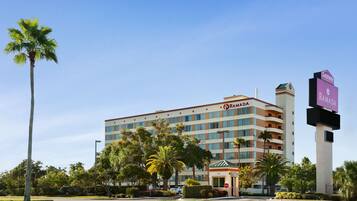 A multi-story hotel with a prominent "Ramada" sign, surrounded by palm trees and a clear sky.