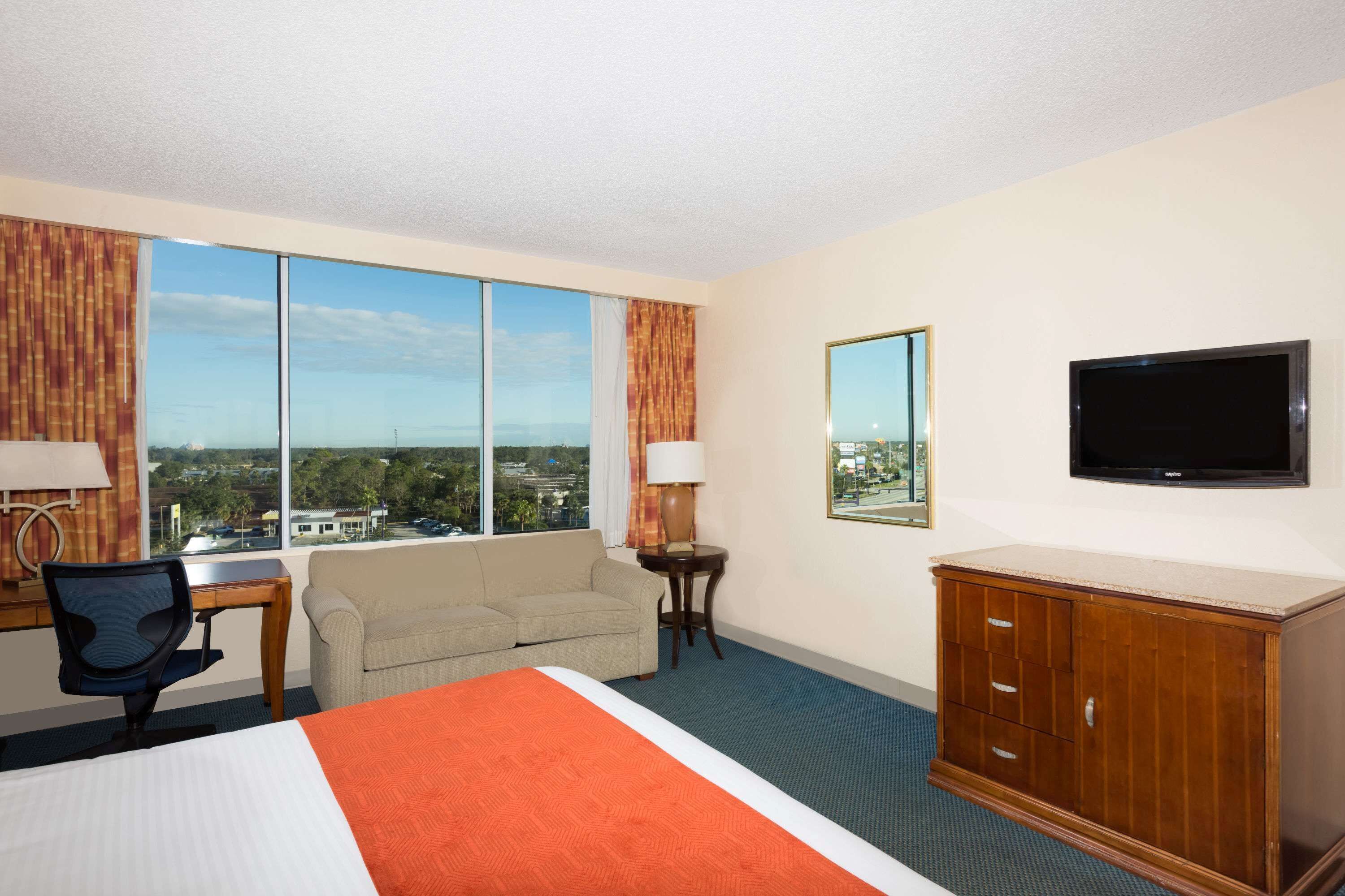 Une chambre d’hôtel dotée d’un grand lit, d’un bureau, d’une chaise, d’un canapé, d’une télévision et offrant une vue sur la ville grâce à de grandes fenêtres.