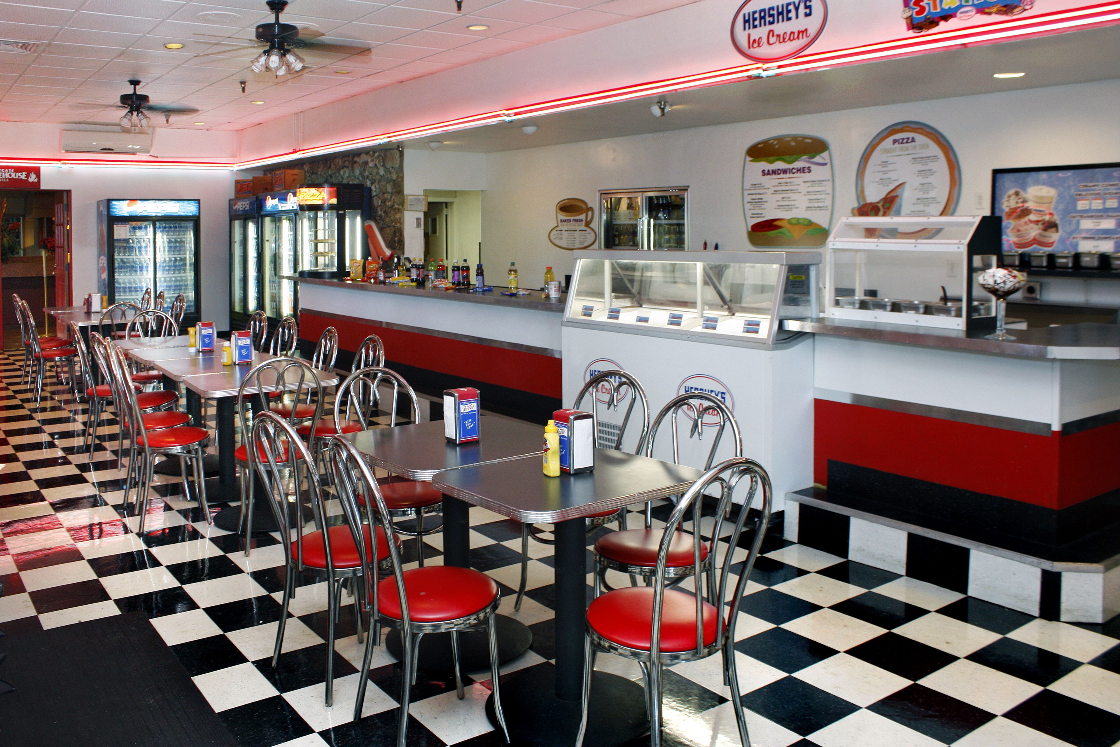 Un restaurante con suelo de cuadros, decoración en rojo y blanco, y una pizarra con el menú.