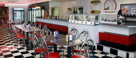 Un restaurante con suelo de cuadros, decoración en rojo y blanco, y una pizarra con el menú.