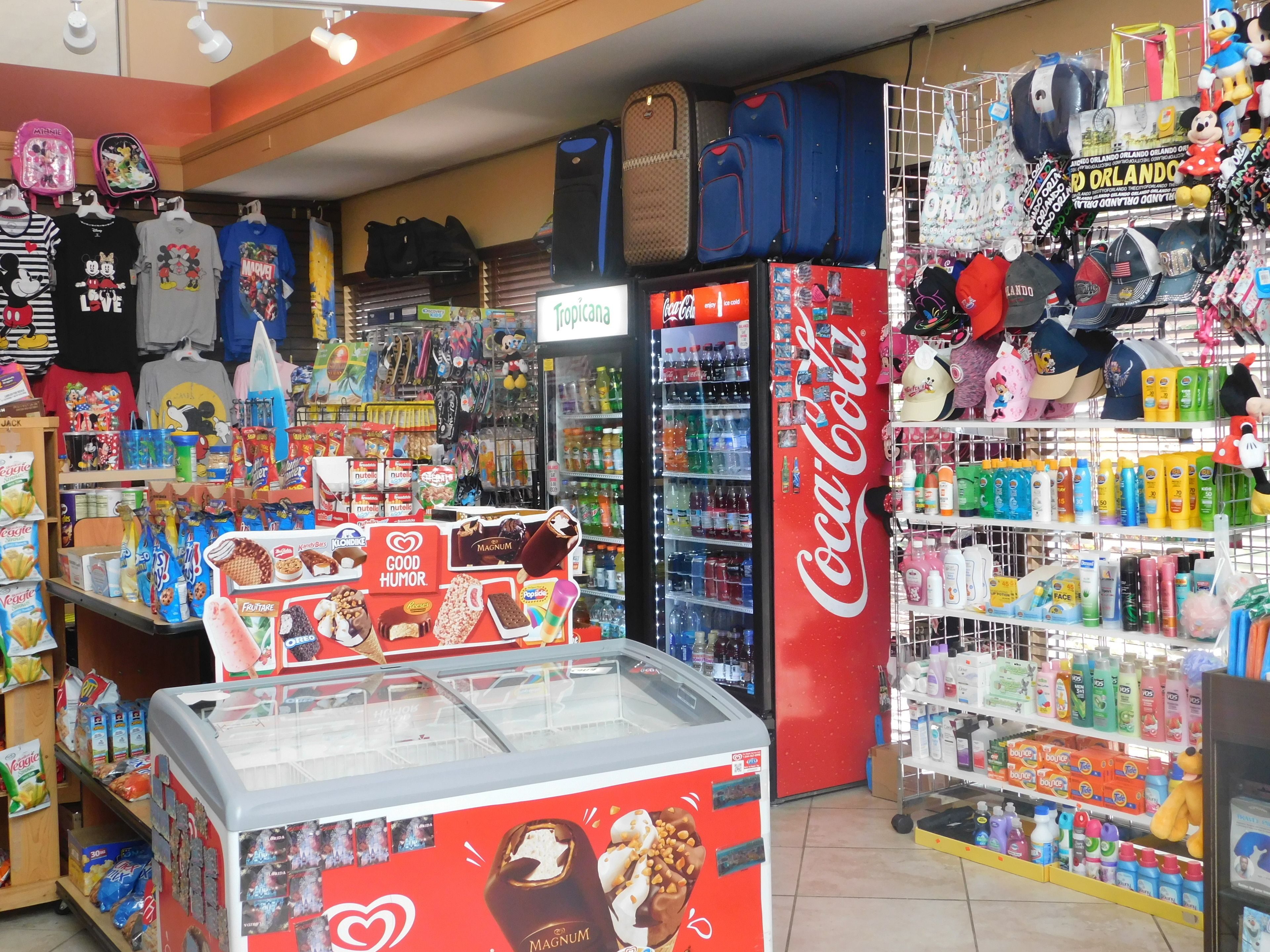 Uma loja de conveniência com refrigerador de Coca-Cola, corredores de lanches e diversos produtos, incluindo bonés e bichos de pelúcia.