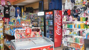 Uma loja de conveniência com refrigerador de Coca-Cola, corredores de lanches e diversos produtos, incluindo bonés e bichos de pelúcia.