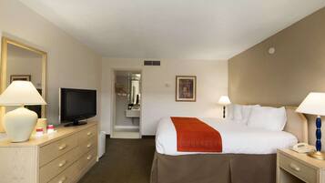 Una habitación de hotel con cama, televisión, escritorio con lámpara, cómoda y espejo.