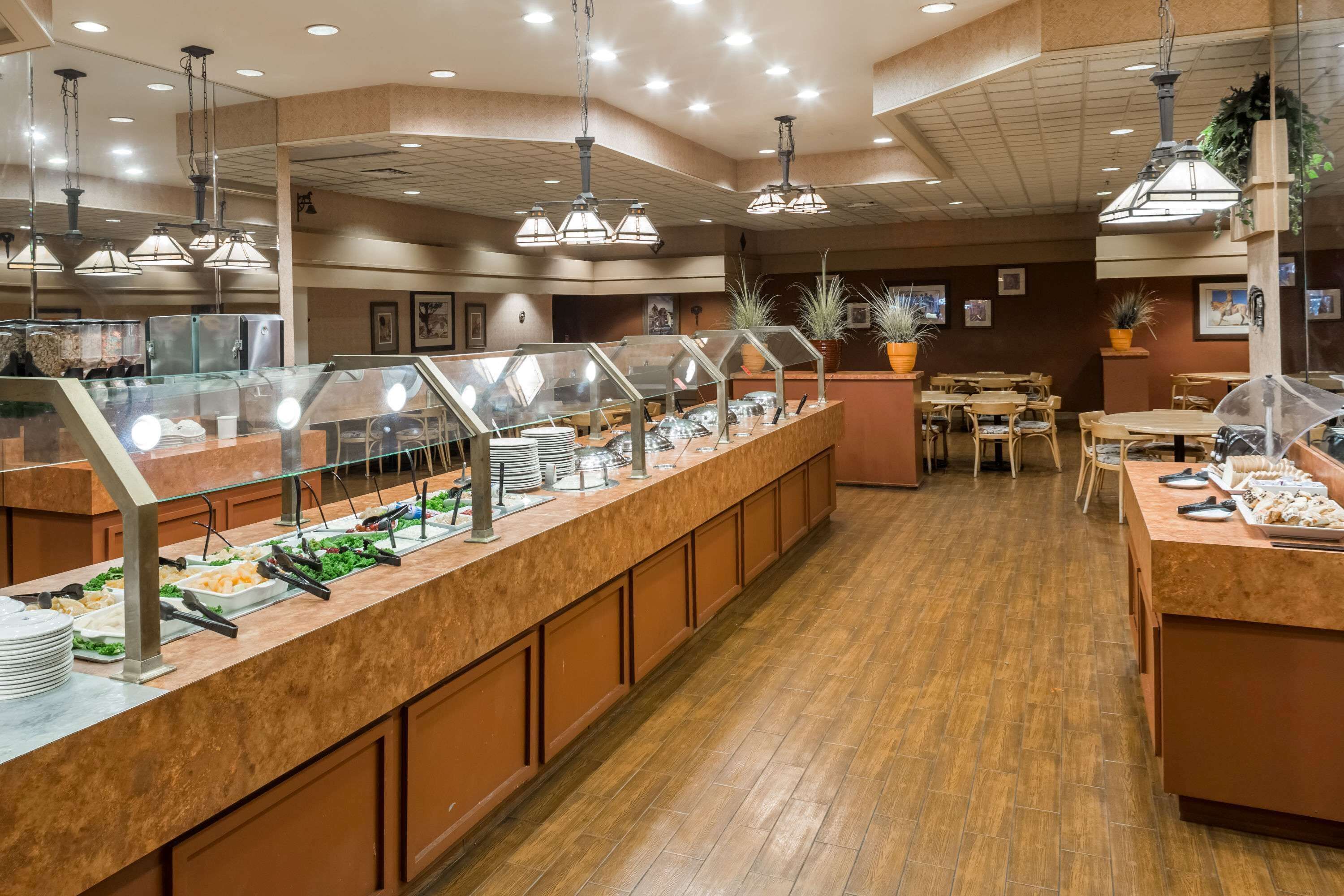 Uma área de buffet com vários pontos de comida, piso de madeira e luminárias pendentes.