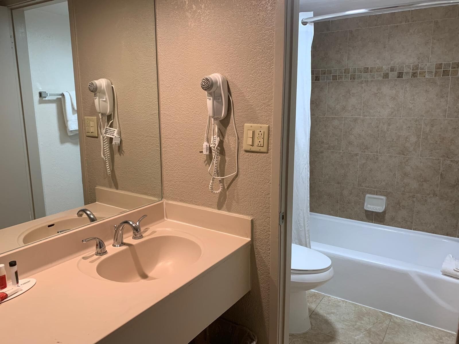 A bathroom with a sink, two hair dryers mounted on the wall, a toilet, and a bathtub.