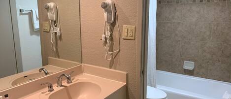 A bathroom with a sink, two hair dryers mounted on the wall, a toilet, and a bathtub.