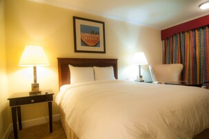 A hotel room with a large bed, two bedside tables with lamps, a chair, and a framed picture on the wall.