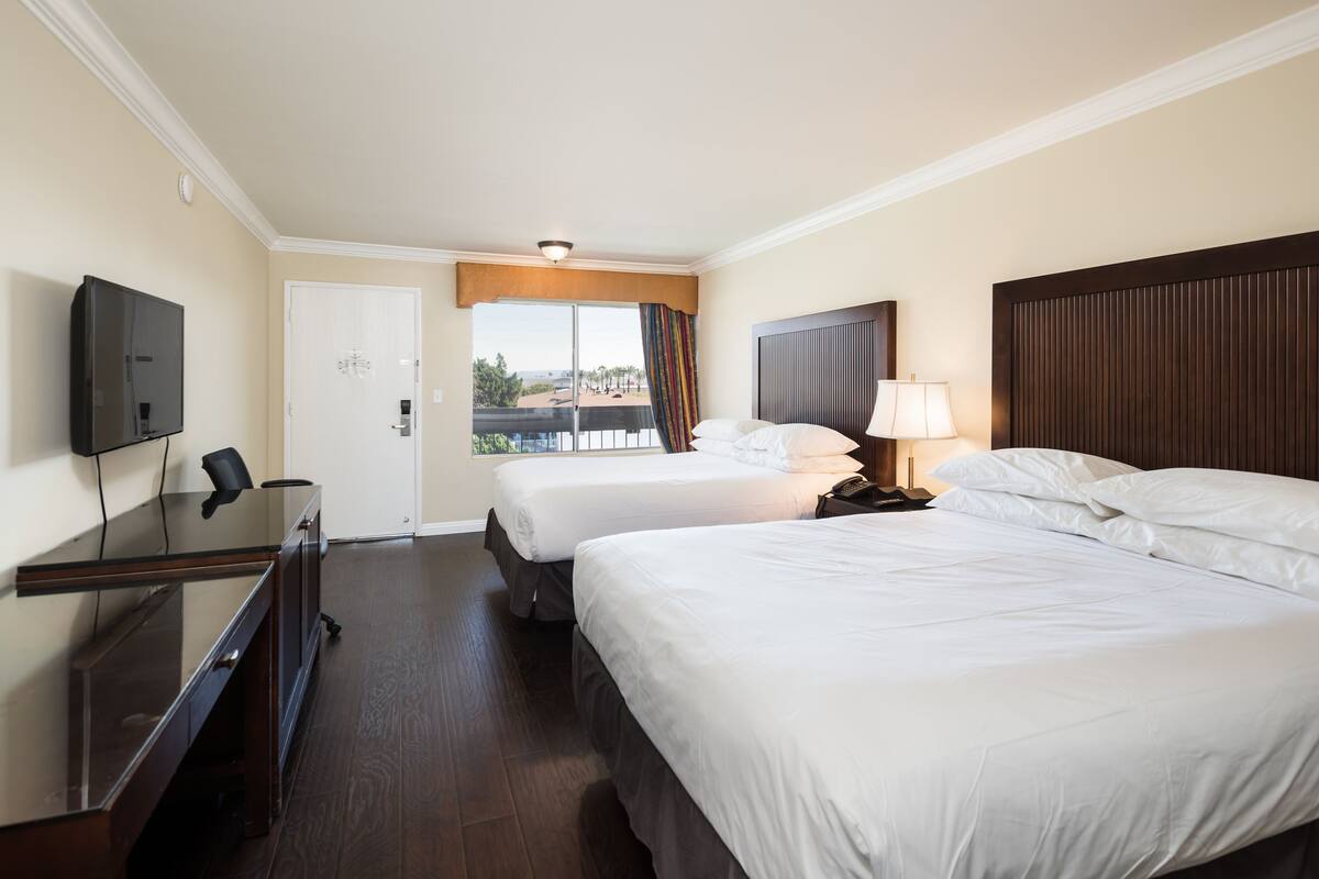 A hotel room with two beds, a TV, a desk, and a balcony view.