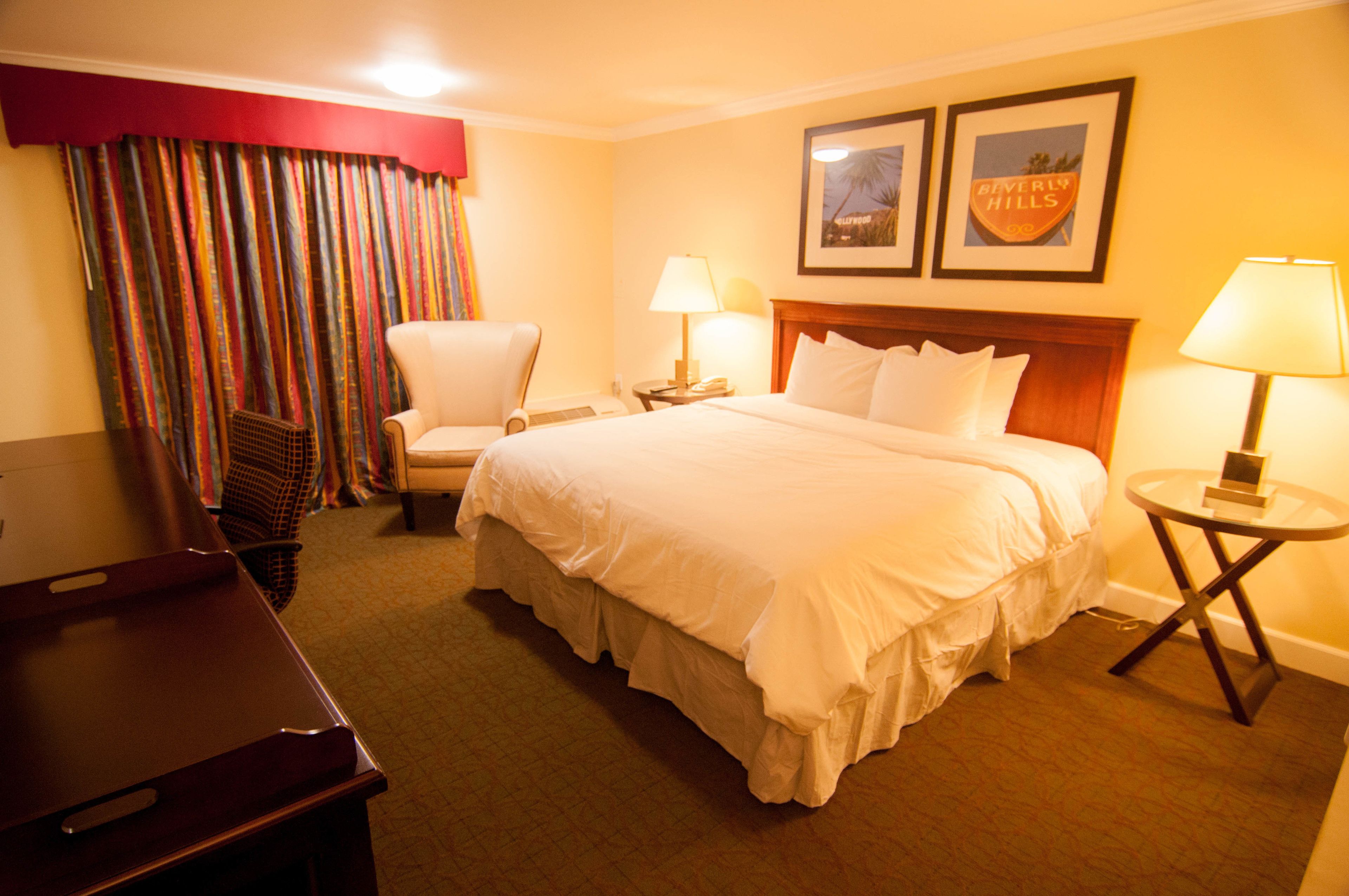 A hotel room with a large bed, a chair, a desk, and a lamp.