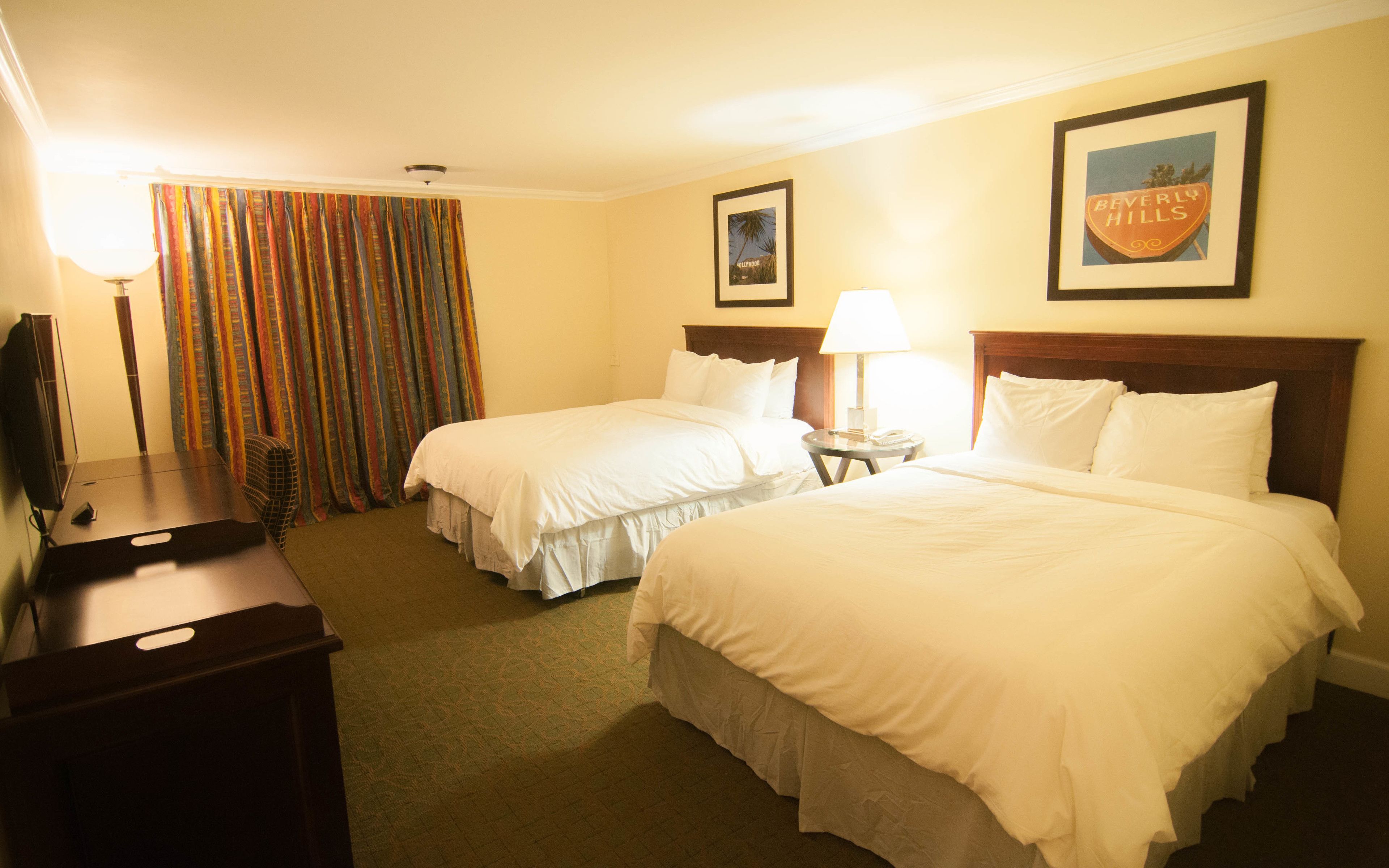 A hotel room with two beds, a desk, a lamp, and a framed picture on the wall.