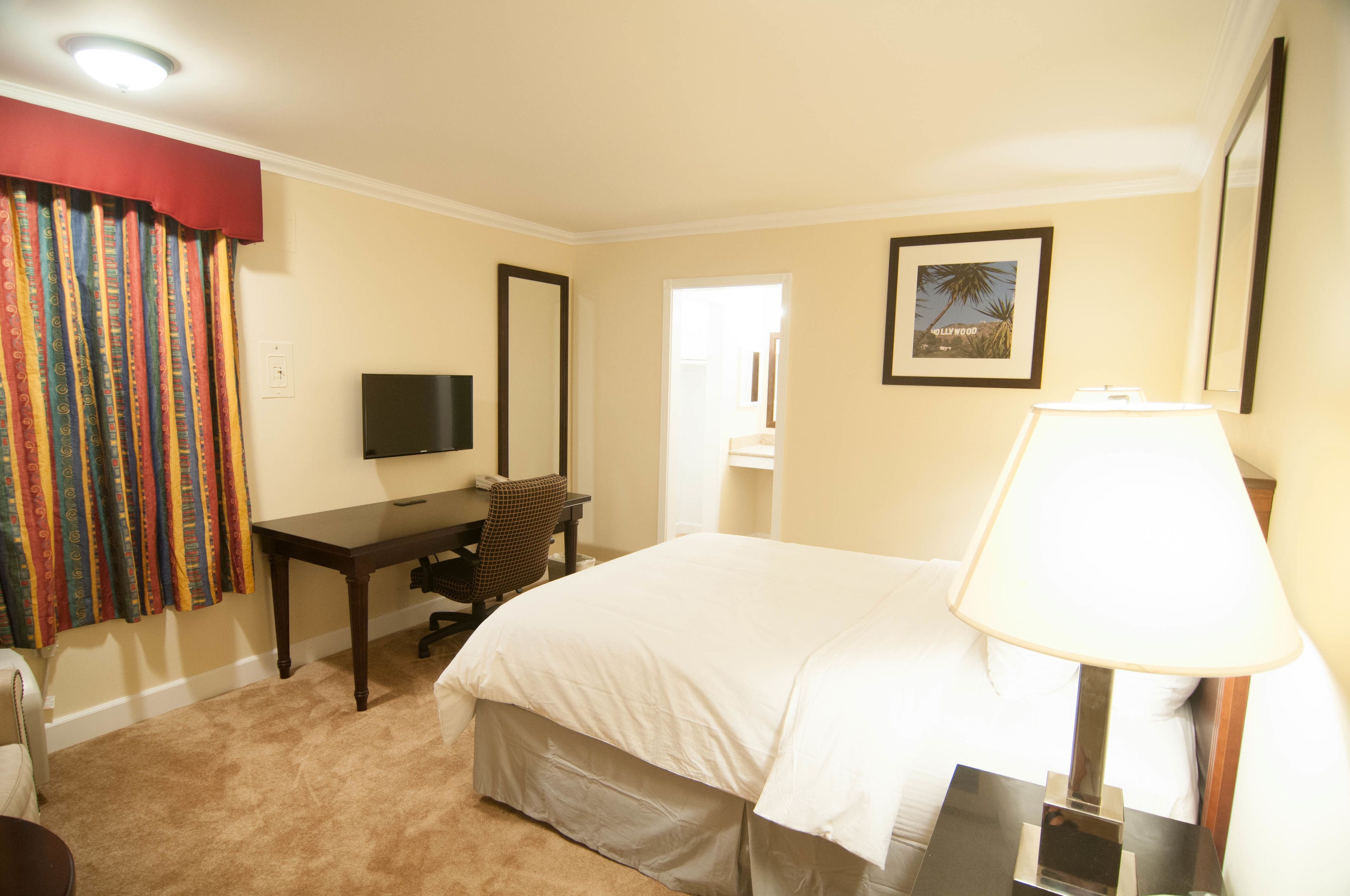 A hotel room with a bed, a desk, a chair, a TV, and a lamp.