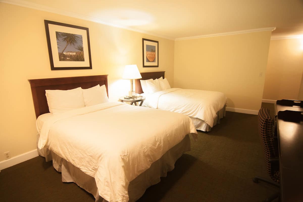 A hotel room with two beds, a nightstand with a lamp, and framed pictures on the wall.