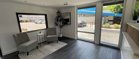 A modern waiting area with a large window, two armchairs, a small table with a vase, and a potted plant.