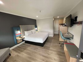 Una habitación de hotel moderna con una cama grande, un escritorio y un televisor.