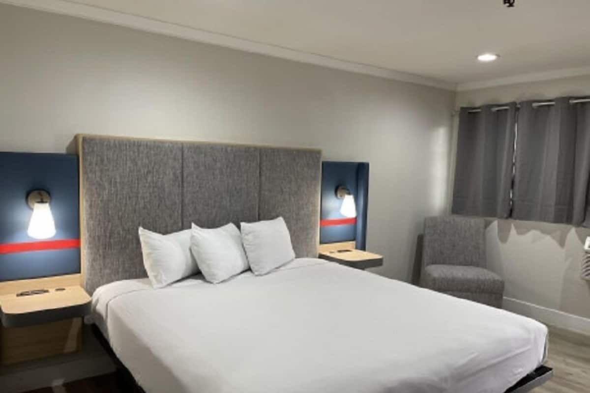Une chambre d’hôtel avec un grand lit, deux tables de chevet, une chaise et une fenêtre avec des rideaux.