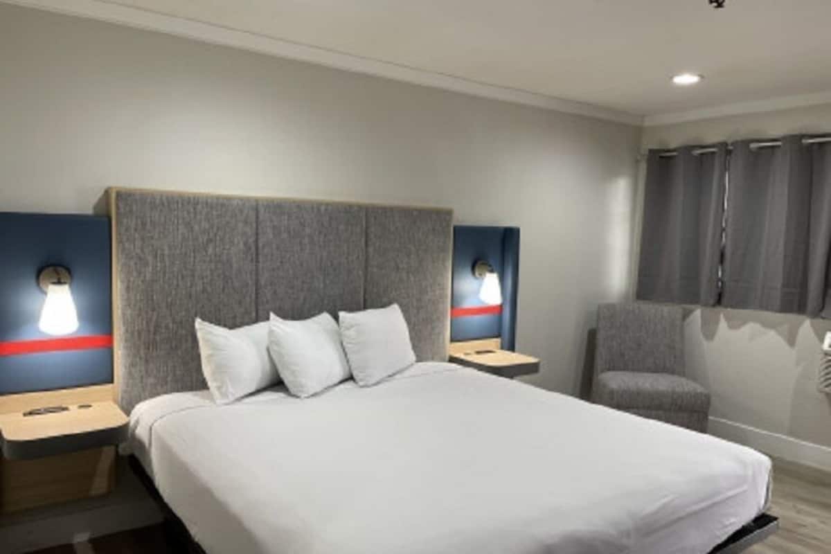 A hotel room with a large bed, two bedside tables, a chair, and a window with curtains.