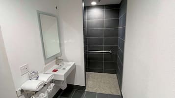 A modern bathroom with a white sink, a mirror, and a shower area with dark tiles.