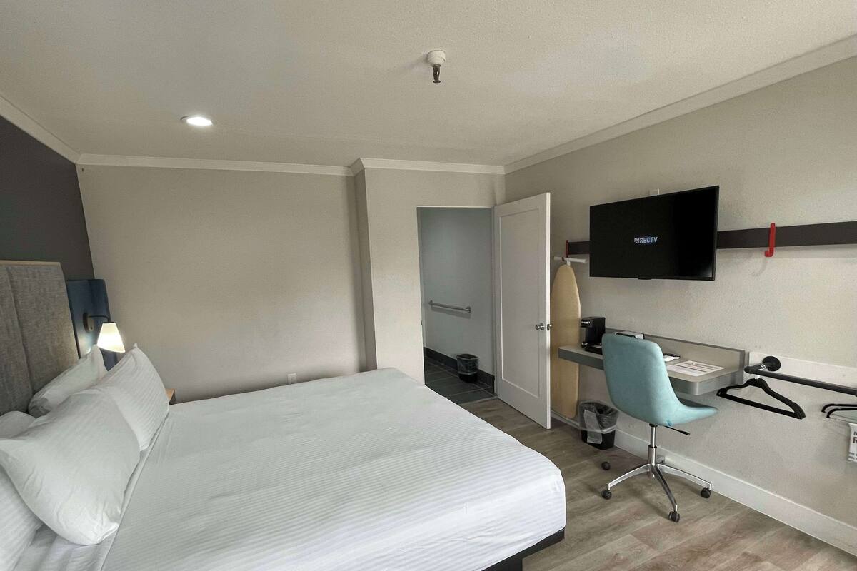 Une chambre d’hôtel moderne équipée d’un grand lit, d’un bureau avec une chaise, d’une télévision et d’une petite planche à repasser.