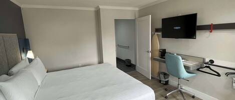A modern hotel room with a large bed, a desk with a chair, a television, and a small ironing board.