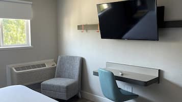 A modern hotel room with a large bed, a desk with a chair, a mounted TV, and a window with blinds.