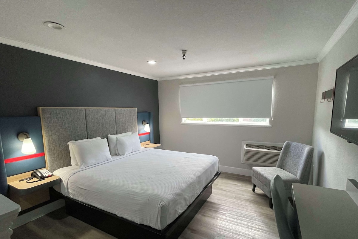 Une chambre d’hôtel moderne dotée d’un grand lit, de tables de chevet avec des lampes, d’une télévision, d’une fenêtre avec des stores et d’un système de climatisation intégré.
