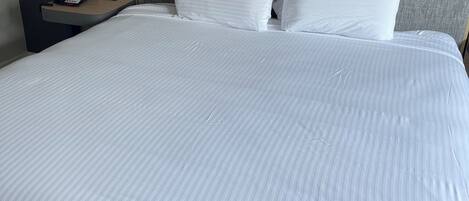Una cama bien hecha con ropa blanca y un cabecero gris.