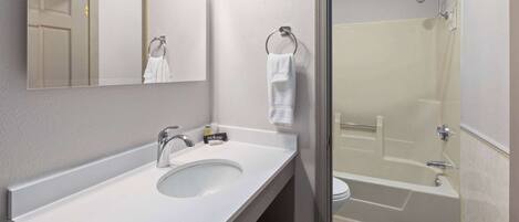 Un baño moderno con lavamanos blanco, espejo, toallero y zona de ducha con mampara de vidrio.