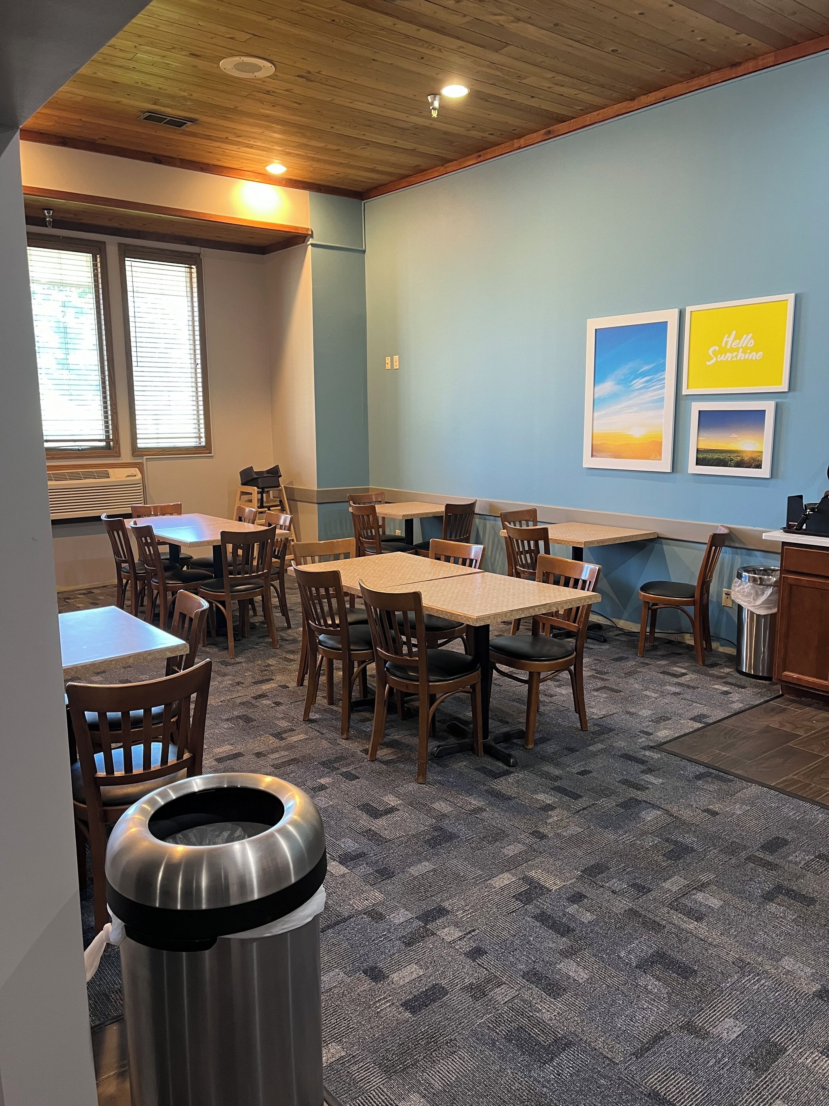 A dining area with multiple tables and chairs, a trash bin, and framed pictures on the wall.