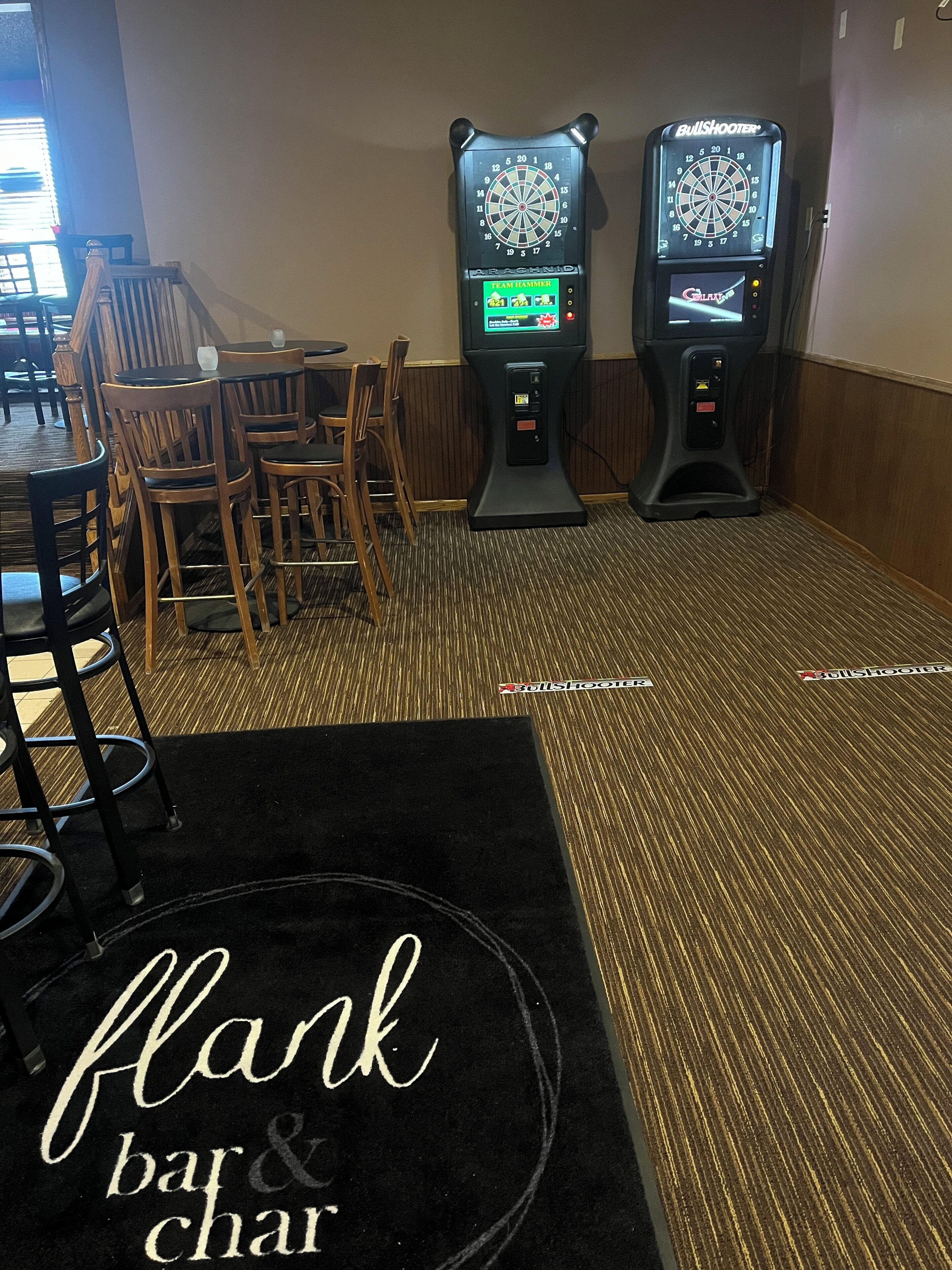A bar area with two dartboards, wooden chairs, and a black carpet with 'flank bar & char' text.