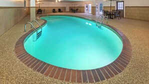 Una piscina interior con borde de azulejos, rodeada de un área de descanso con sillas y una mesa.