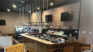 Una zona de bar con mostrador de madera, taburetes y pared de ladrillo.