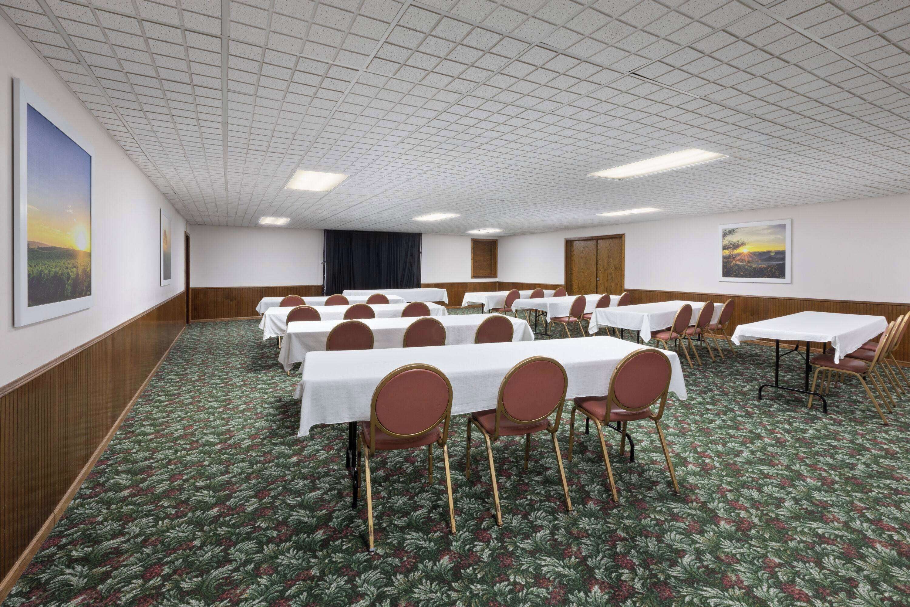 A conference room with multiple tables and chairs, a patterned carpet, and framed pictures on the walls.