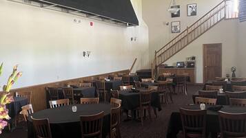 A restaurant with round tables and wooden chairs, a staircase, and a black awning with the name "Flank".