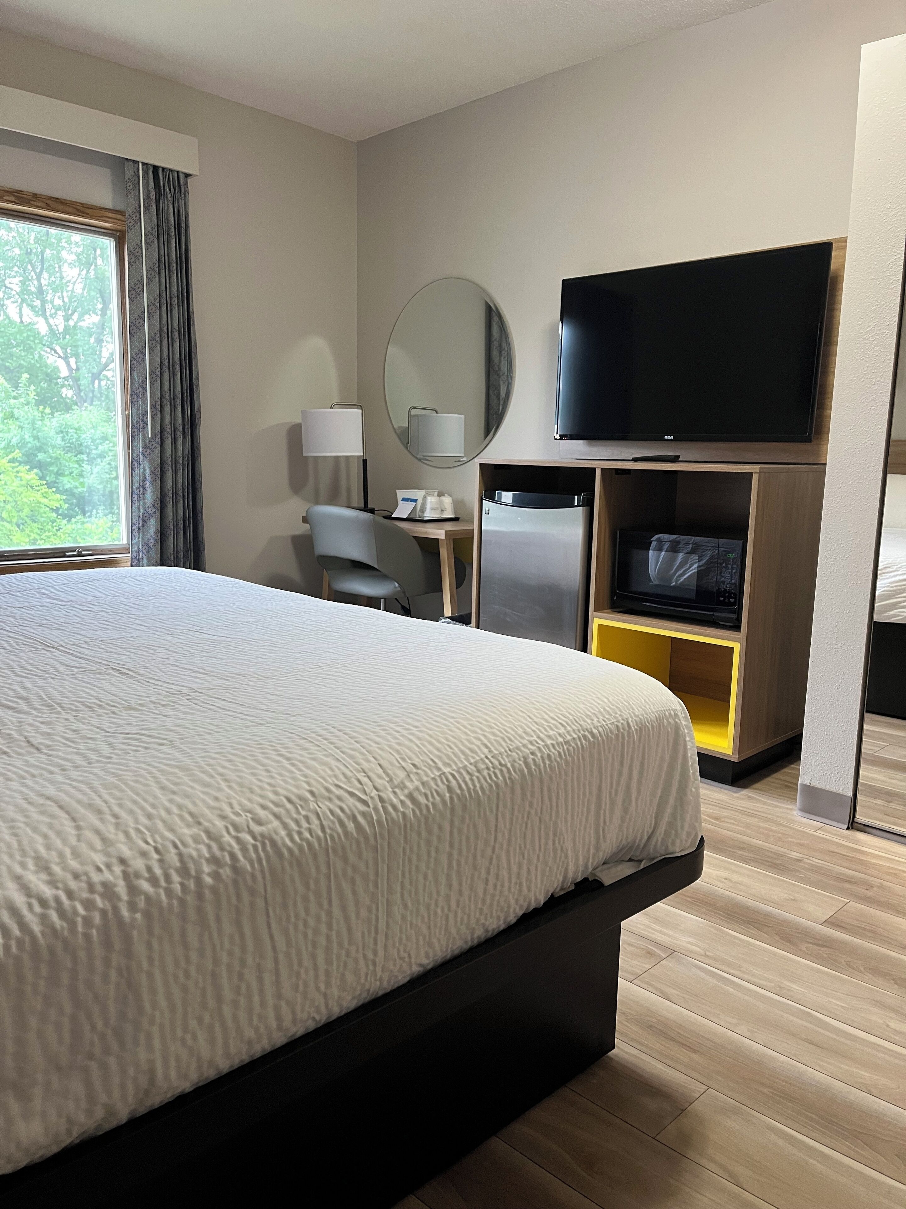 A hotel room with a large bed, a flat-screen TV, a desk with a lamp, a microwave, and a refrigerator.