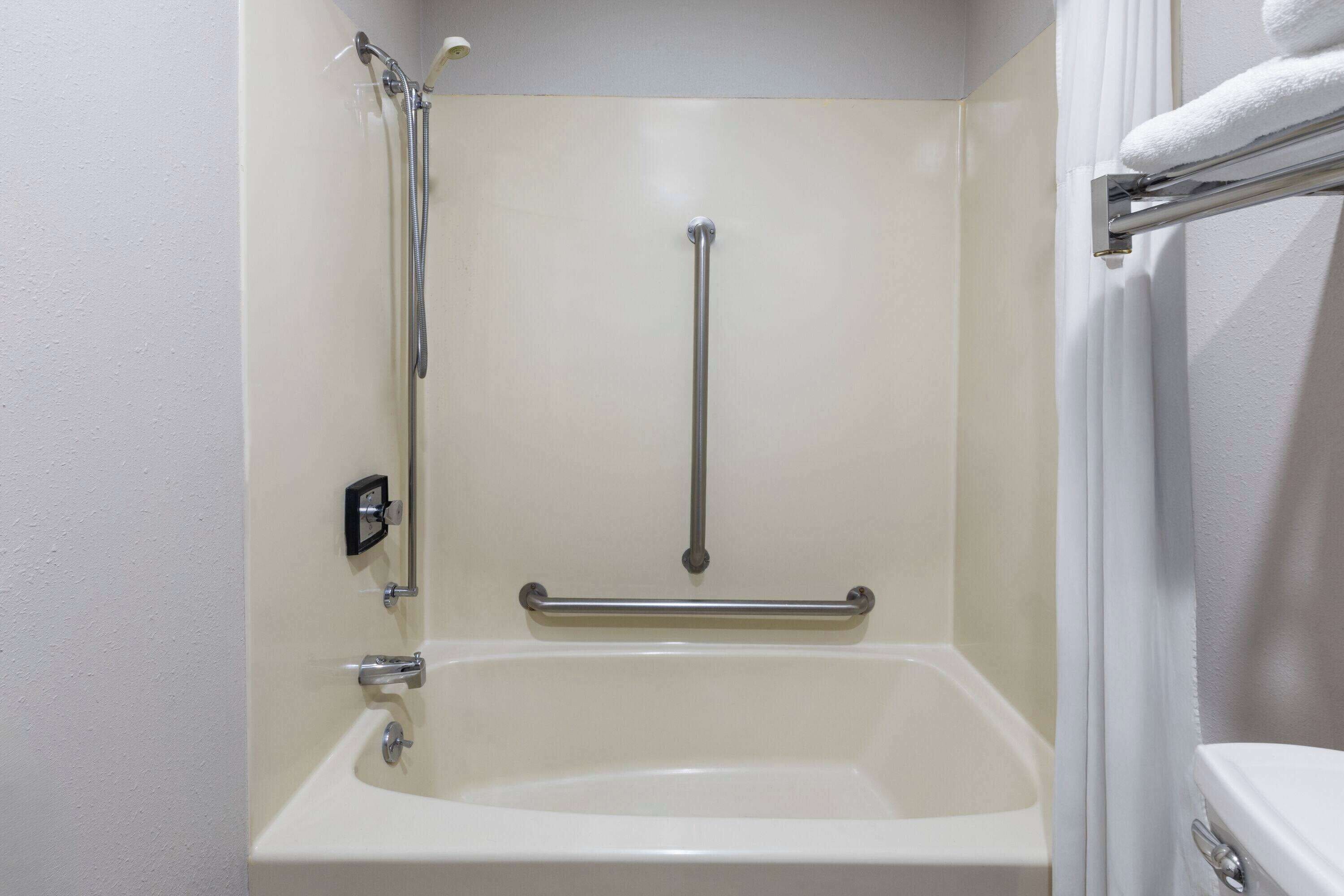 A bathroom with a bathtub, a shower with a grab bar, and a toilet.