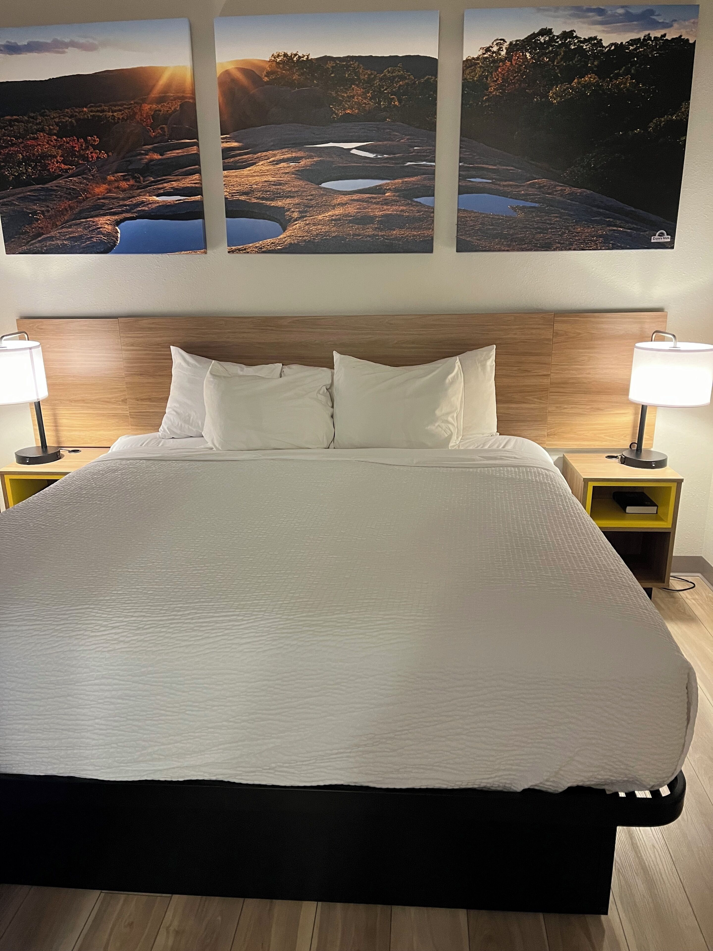A neatly made bed with white bedding, two bedside tables with lamps, and a wooden headboard.