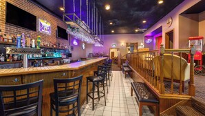 Zona de bar con mostrador de madera, varios taburetes y una gran variedad de botellas.