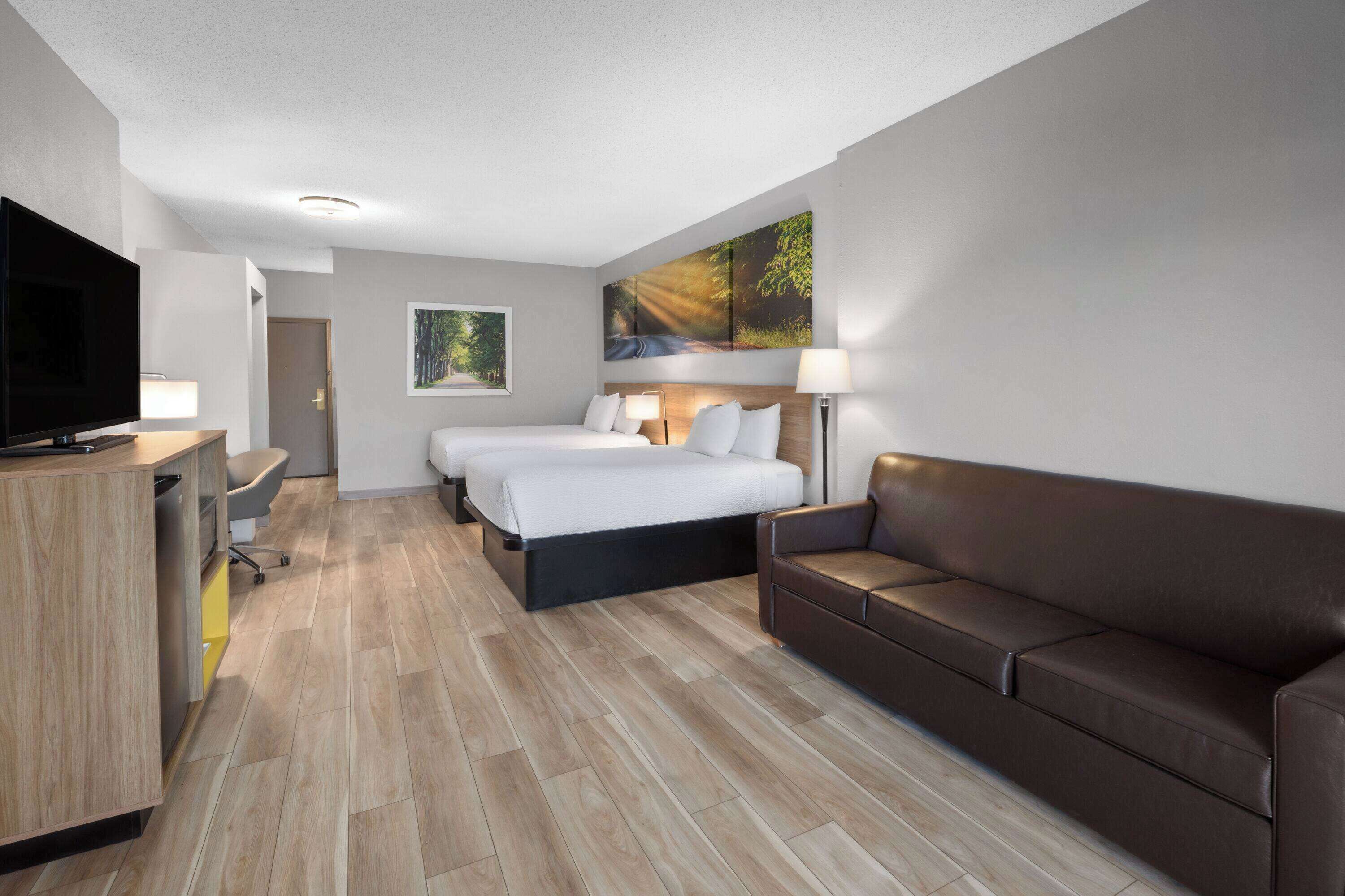 Ein Hotelzimmer mit einem Bett, einer Couch, einem Schreibtisch mit Fernseher und einem Bild an der Wand.