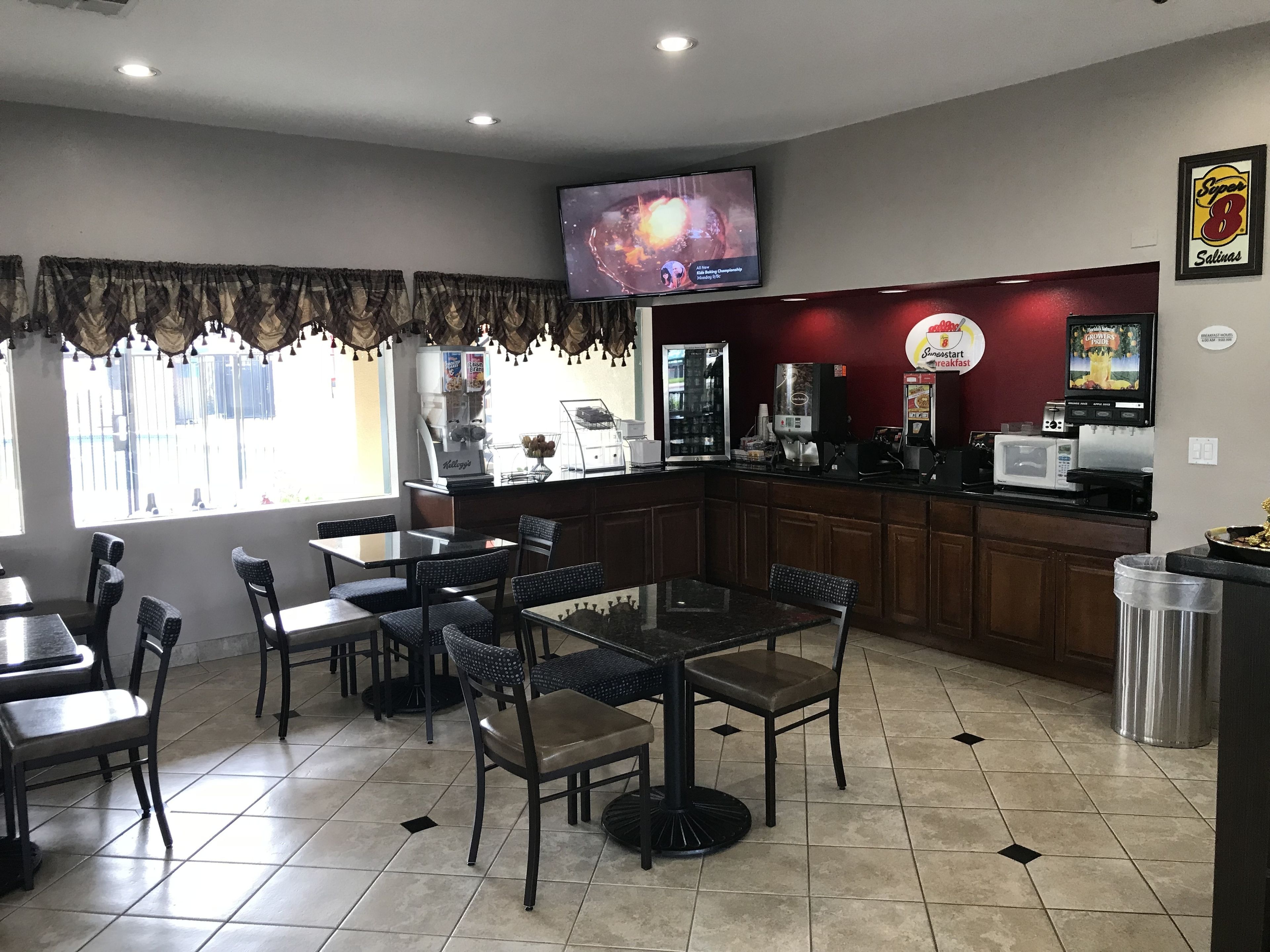 A restaurant with a counter, tables, chairs, a television, and a coffee machine.